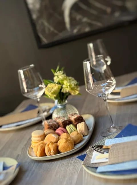 Formal place setting with macaron desserts, wine glass, yellow flowers in vase, and blue napkins on wooden table