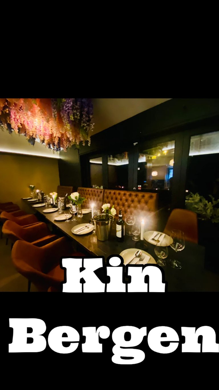 Upscale restaurant dining room with long table, orange chairs, elegant place settings, decorative floral ceiling installation