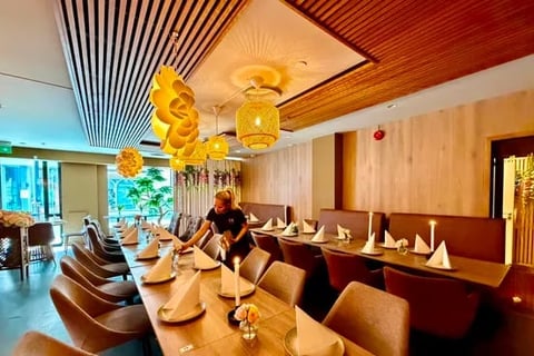 Modern fine dining restaurant interior with long wooden table, beige chairs, decorative gold balloon sculptures, and warm ambient lighting