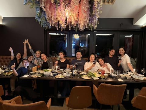 Group of people dining together at a long table with hanging floral decoration overhead in an upscale restaurant