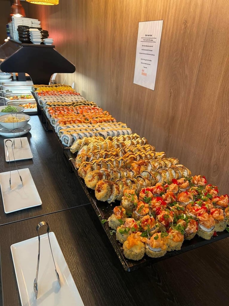 Long buffet table display of various colorful sushi rolls in rows on black platters