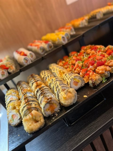 Assorted sushi rolls on black platter including spicy tuna, rainbow, and tempura varieties