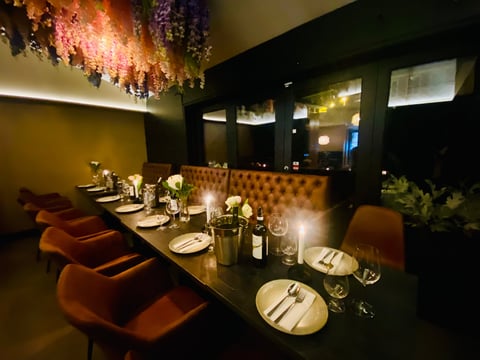 Upscale restaurant private dining room with orange velvet chairs, black table, place settings, and decorative hanging floral arrangement