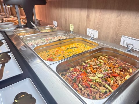Buffet line with stainless steel warming trays containing pasta and vegetable medley