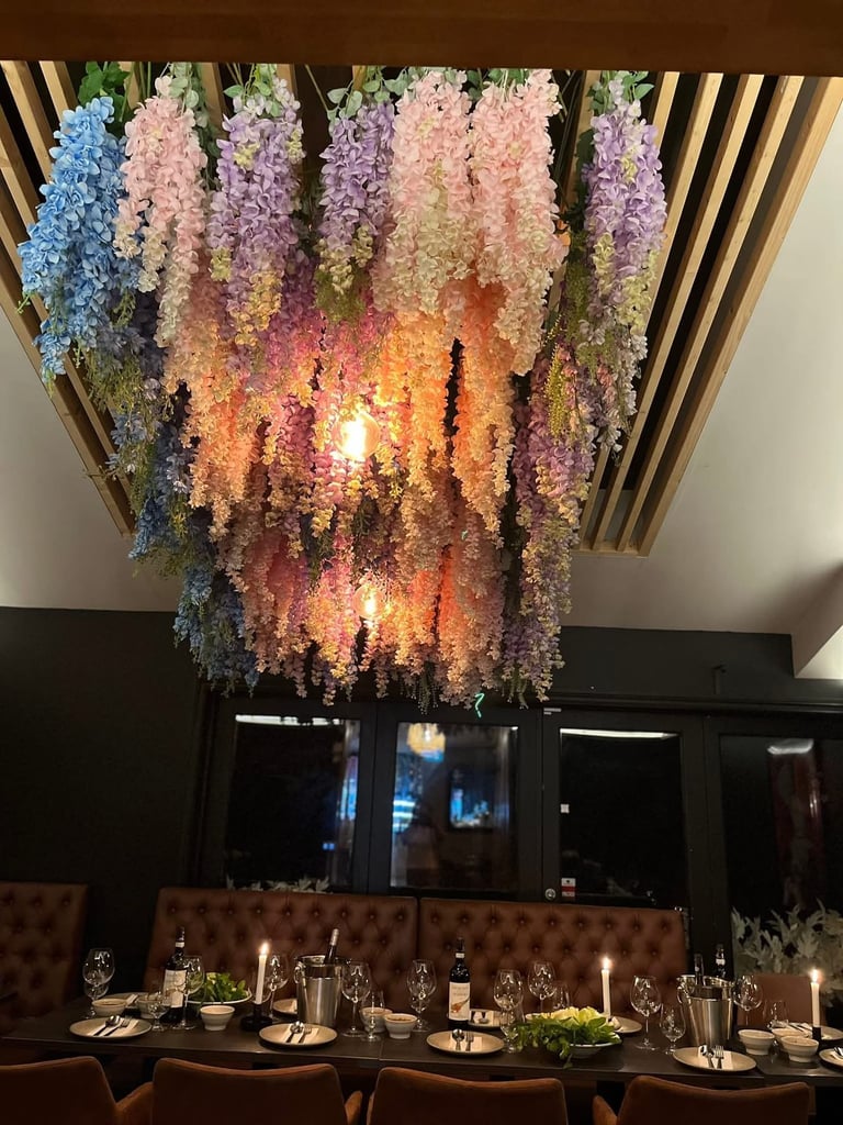 Elegant dining room with hanging floral installation featuring cascading flowers in pink, purple, blue, and orange tones