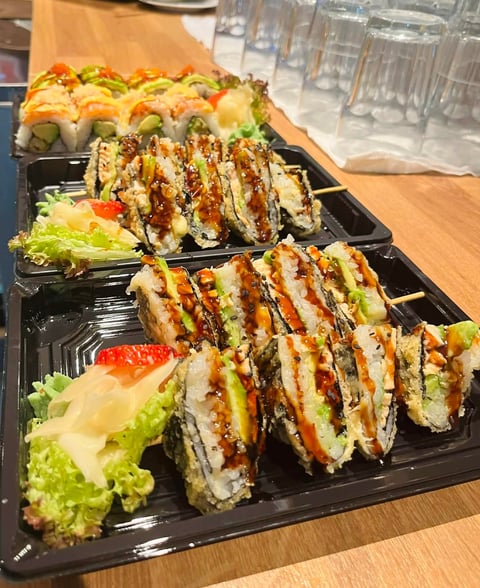 Assorted sushi rolls with drizzled sauce on black platter with lettuce garnish